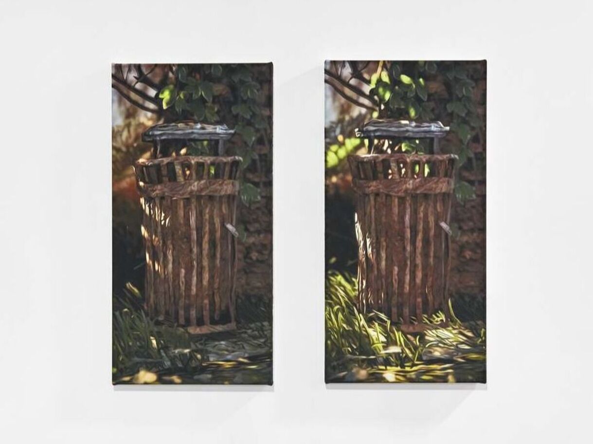 A photo of two similar paintings a on wall next to each other. The paintings are of a brown cylinder object, possibly made from metal or wood but very old and worn. The object is located in a wood or natural landscape with grass on the floor and leaves in the background. One image has sunlight making shadows in the foreground. 
